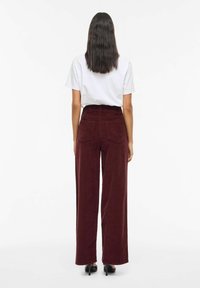 Wijd uitlopende bordeauxrode ribfluwelen broek met een hoge taille, achterzakken en een gladde textuur, gecombineerd met een wit T-shirt.