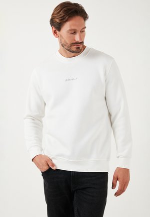 Fehér, pamut keverék anyagból készült pulóver, kerek nyakkivágással, hosszú ujjakkal és egy kis szürke logóval a mellrészen.