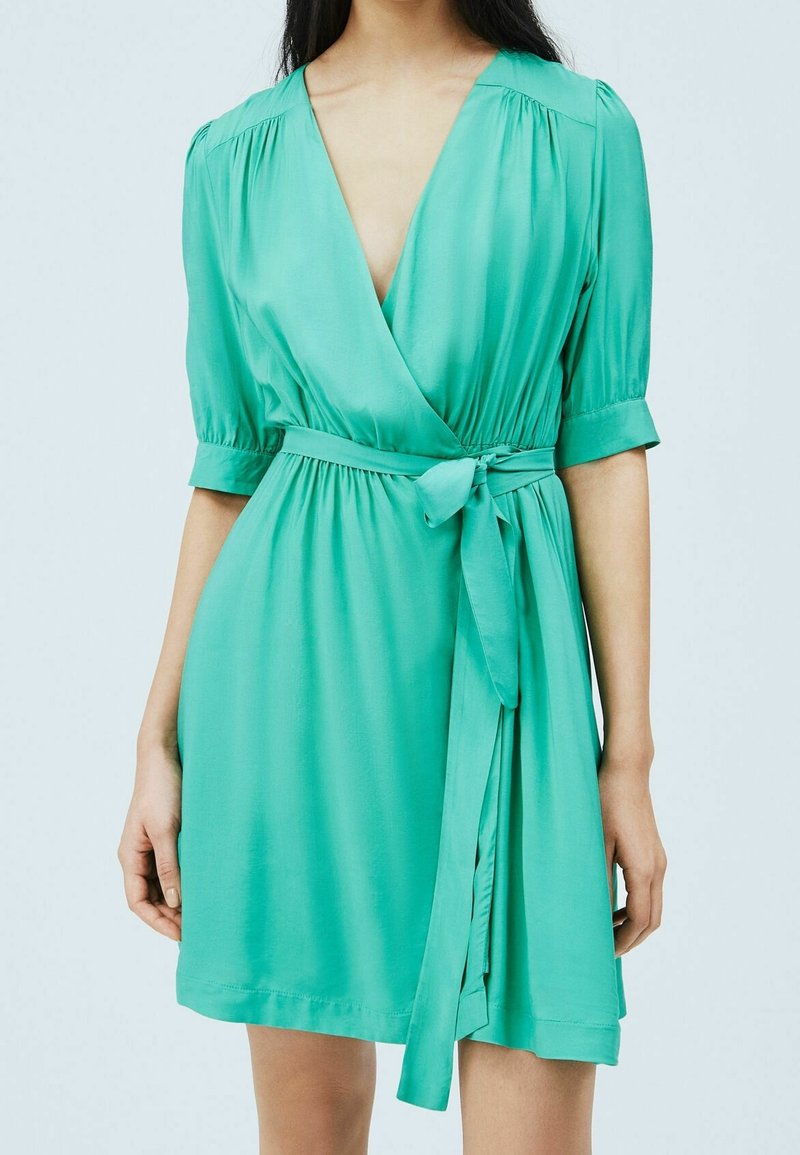 Robe portefeuille verte en tissu satiné, avec des manches courtes, un décolleté en V profond et une ceinture à la taille pour un ajustement personnalisé.