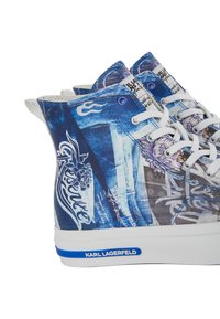 Aukštos sportbačiai su mėlynu grafiniu raštu, baltais raišteliais, tekstūruota paviršiumi ir baltu padu su mėlyna logotipo akcentu.