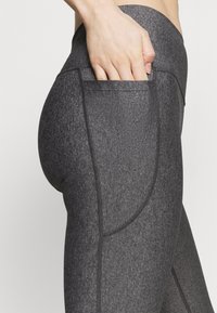 Leggings da allenamento grigi con una finitura liscia e strutturata, una vita alta e una tasca laterale integrata nel design.