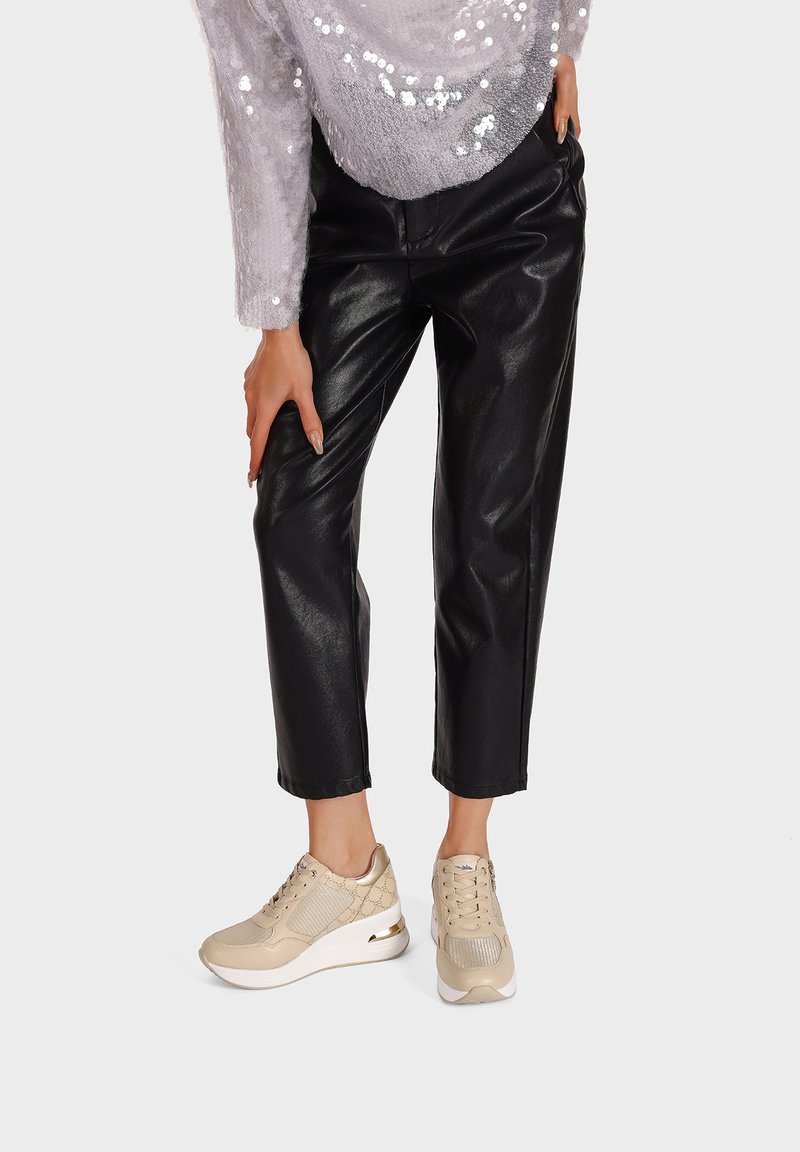 Sneakers beige con mesh testurizzato e pelle liscia, dotati di una suola bianca e di un branding discreto, abbinate a pantaloni neri in ecopelle.