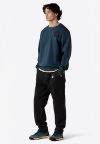 Mørkeblå sweatshirt med en tekstureret finish, der har en grå rund halsudskæring og en frontlomme. Kombineret med sorte bukser og sko med blå accenter.