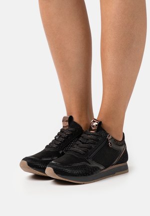 Schwarze Sport Schuhe mit einem strukturierten Mesh-Obermaterial, metallischen Akzenten und einem Design, das einen Reißverschluss an der Seite enthält.