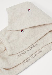 Šviesiai bežinė medvilninė skara, turinti subtilią tekstūrą, sulankstyta su mažu raudonu, baltu ir mėlynu logotipu bei siuvinėtu kraštu "TOMMY HILFIGER".