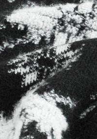 Tissu tricoté noir et blanc avec une surface texturée et floue, présentant un motif complexe de formes géométriques et un contraste doux.