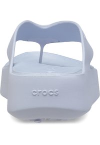 Sandales Crocs blanches avec une large sangle, semelle rembourrée et forme ergonomique. Présente un logo en relief sur le côté et une sangle texturée.