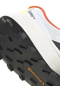 Nahaufnahme der Sohle eines weißen und orangefarbenen Terrex-Wanderschuhs mit schwarzem Continental-Gummiprofil für verbesserten Grip und Langlebigkeit.