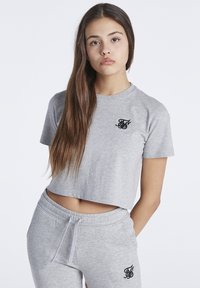 Camiseta corta gris con mangas cortas y detalle del logo negro en el pecho, combinada con pantalones de chándal gris a juego que también cuentan con un logo.