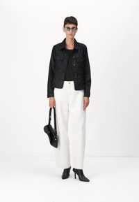 Giacca di denim nera sopra un top nero, pantaloni bianchi a gamba larga e stivali neri con tacco. Gli accessori includono una borsa nera a tracolla e occhiali da sole.