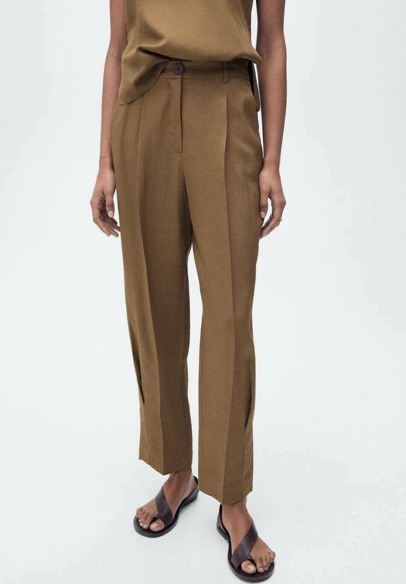Pantalons marron ajustés avec plis, présentant une coupe droite et des fentes latérales à l'ourlet. Associés à un haut assorti et des sandales plates.