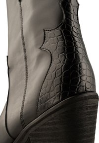 Stivale in pelle nera con un accento in pelle di rettile testurizzata, un tacco a zeppa scolpito e dettagli decorativi delle cuciture lungo il lato.