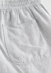 Light grey linen shorts featuring an elastic waistband and a back pocket with a curved hem. Texture appears soft and woven.