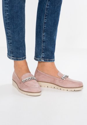 Fødder iført lyserøde ruskindsløbere med dekorative sølvperler på toppen, parret med blå denimjeans.
