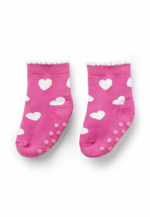 Rosa Babysocken mit weißen Herzmustern und rutschfesten Gummigriffen auf der Sohle, vor einem weißen Hintergrund.