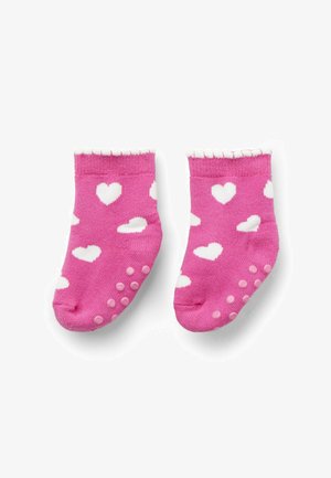 Chaussettes de bébé roses avec des motifs de cœurs blancs et des grips en caoutchouc antidérapants sur les semelles, sur un fond blanc.