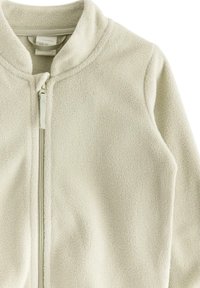Giacca in pile beige chiaro con colletto alto, zip completa e texture morbida. Presenta un design semplice senza motivi o accenti visibili.
