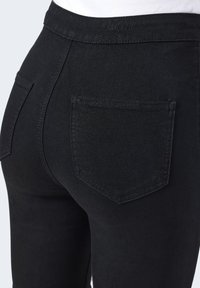Jeans de mezclilla negra de cintura alta con una forma ajustada, que presentan un único bolsillo trasero y una textura suave.