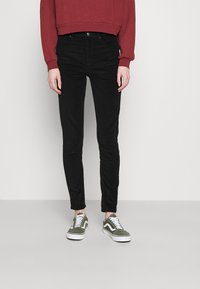 Černé skinny džíny v kombinaci s kráceným vínovým svetrem. Obuv zahrnuje zelené a bílé tenisky. Jednoduchý, neformální outfit s přiléhavým siluetou.