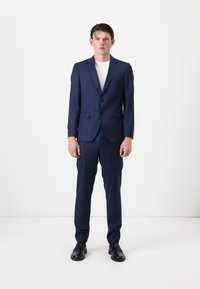 Traje de marina con hombros estructurados, chaqueta ajustada y pantalones de corte recto. Un par de zapatos de cuero negro con textura suave y diseño minimalista.