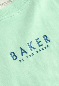 Svetlozelené tričko s krátkym rukávom a mäkkou textúrou, s výrazným modrým nápisom "BAKER" a menším nápisom "by TED BAKER" pod ním.