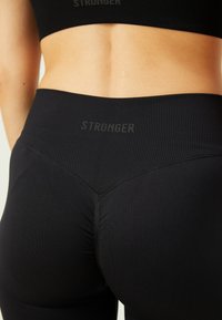 Leggings negras con relieve y una cinturilla alta que presenta el texto "STRONGER" en una fuente sutil, enfatizando un diseño ajustado y texturizado.