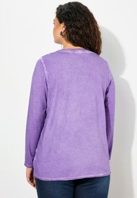 Violettes Langarmshirt aus einem weichen, strukturierten Stoff mit lockerer Passform und abgerundetem Saum, ausgestattet mit einem Rundhalsausschnitt und einem dezenten Verblassungsmuster.