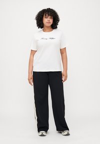 Witte t-shirt met korte mouwen met "Tommy Hilfiger" in zwarte script, gecombineerd met zwarte wijde broek met zijstrepen.
