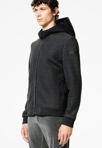 Giacca a zip da uomo in misto lana grigio scuro con cappuccio imbottito nero, orlo a costine, tasche laterali e cuciture piatte. Texture liscia e design moderno.