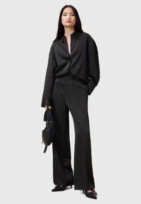 Camicia nera in satin con vestibilità rilassata, apertura frontale con bottoni e colletto profondo; pantaloni neri a gamba larga con finish liscio e pieghe sottili.