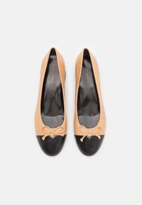 Bailarinas con parte superior de cuero nude y puntera de cuero negro. Presentan un pequeño lazo y un acento de logo dorado en el lazo.