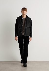 Dark denim jacket with a button front, two front pockets, and a soft collar, paired with black pants and black shoes.