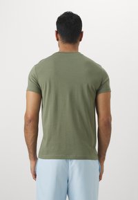 Olive green short-sleeve t-shirt with a crew neck and smooth texture, worn with light blue shorts. No visible patterns or graphics.