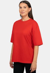Maglietta rossa a maniche corte realizzata in un tessuto misto cotone, con scollatura rotonda e vestibilità rilassata, abbinata a leggings neri.