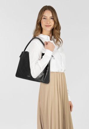 Borsa a spalla nera trapuntata con texture liscia, dotata di un logo e di una forma strutturata. Portata da una persona con una camicia bianca e una gonna beige.