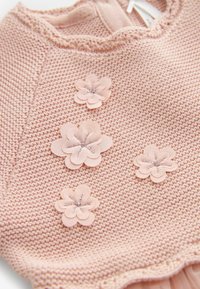 Stickad rosa plagg med en strukturerad mönster, prydd med fem tygblommor, var och en med silverbroderade detaljer.