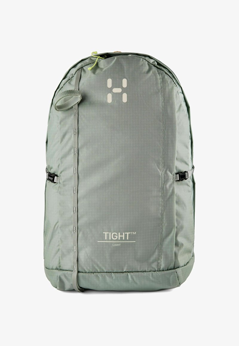 Mochila de tela gris claro con correa vertical frontal, hebillas de compresión laterales y etiqueta "TIGHT™ LIGHT".