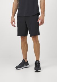 Svarta sportshorts med en lös passform, tillverkade av lätt material, tillsammans med svarta löparskor med vita accenter och logotyp.