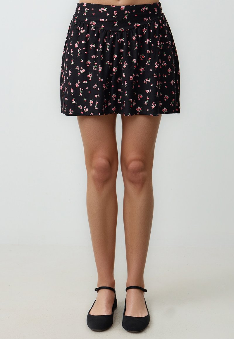 Schwarzer Rock mit floralem Muster und gerafftem Bund, der mit kleinen, rosa Blumen verziert ist. Hergestellt aus einem weichen, leichten Stoff, hat er eine ausgestellte Silhouette.