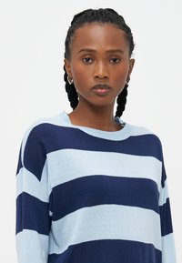 Pulôver riscado em azul-claro e marinho em material de malha suave, com decote redondo e corte solto, com ombros caídos.