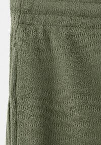 Gros plan sur un tissu tricoté vert olive avec une texture côtelée et des détails de couture le long du bord et de la ceinture.