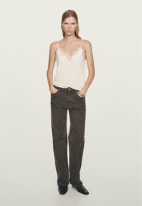 Camisole beige avec dentelle, associé à un pantalon large marron foncé. La tenue présente des lignes simples et une texture lisse, complétée par des chaussures noires.