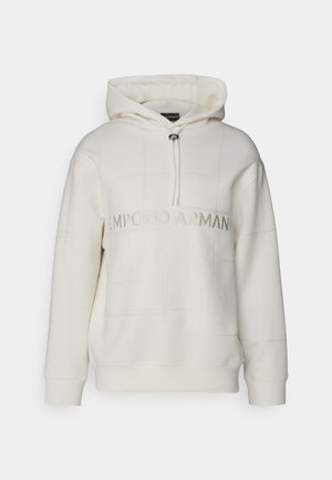 La sudadera color hueso cuenta con un cuello con cordón, un patrón de cuadrícula cosido y un logotipo central. Está hecha de una tela suave con puños de canalé.