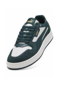 Grøn ruskind og hvid læder sneaker med rundt tå, tyk hvid sål og fremtrædende brandlogo på tungen og siden.