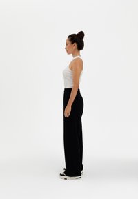 Black wide-leg pants, white fitted tank top, and chunky black sneakers. Side profile view against a plain white background.