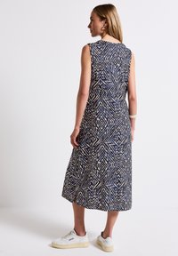 Sleeveless mid-length dress in navy and cream geometric pattern, light fabric, relaxed fit, with a slit at the back, paired with white sneakers.