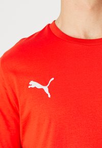 Rode katoenen T-shirt met een wit Puma-logo op de linkerkant van de borst, ronde halslijn en korte mouwen met een gladde textuur.