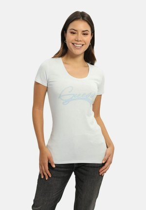Hvid kortærmet t-shirt med rund halsudskæring, prydet med et lysblåt "Guess" design i en glitrende tekstur. Bæres sammen med mørke jeans.