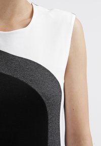 Sukienka w blokowe kolory z czarnymi, szarymi i białymi panelami, o gładkiej fakturze i konstrukcyjnym, bezrękawnikowym kroju.