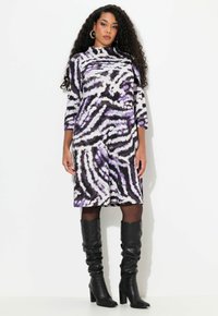 Lila und schwarze zebra-gestreifte Kleid mit hochgeschlossenem Kragen, dreiviertel Ärmel und ausgestellt geschnitten, kombiniert mit schwarzen kniehohen Stiefeln.